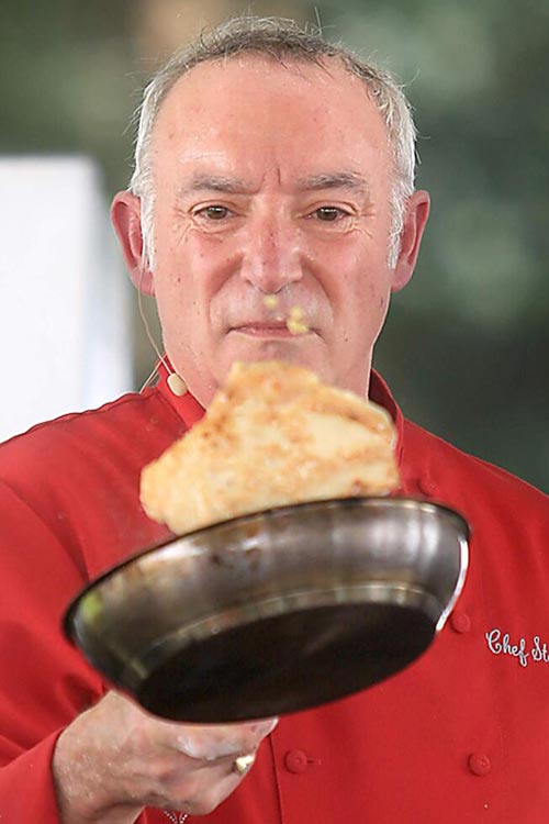 Chef in a red uniform holds a pan with a large crepe.